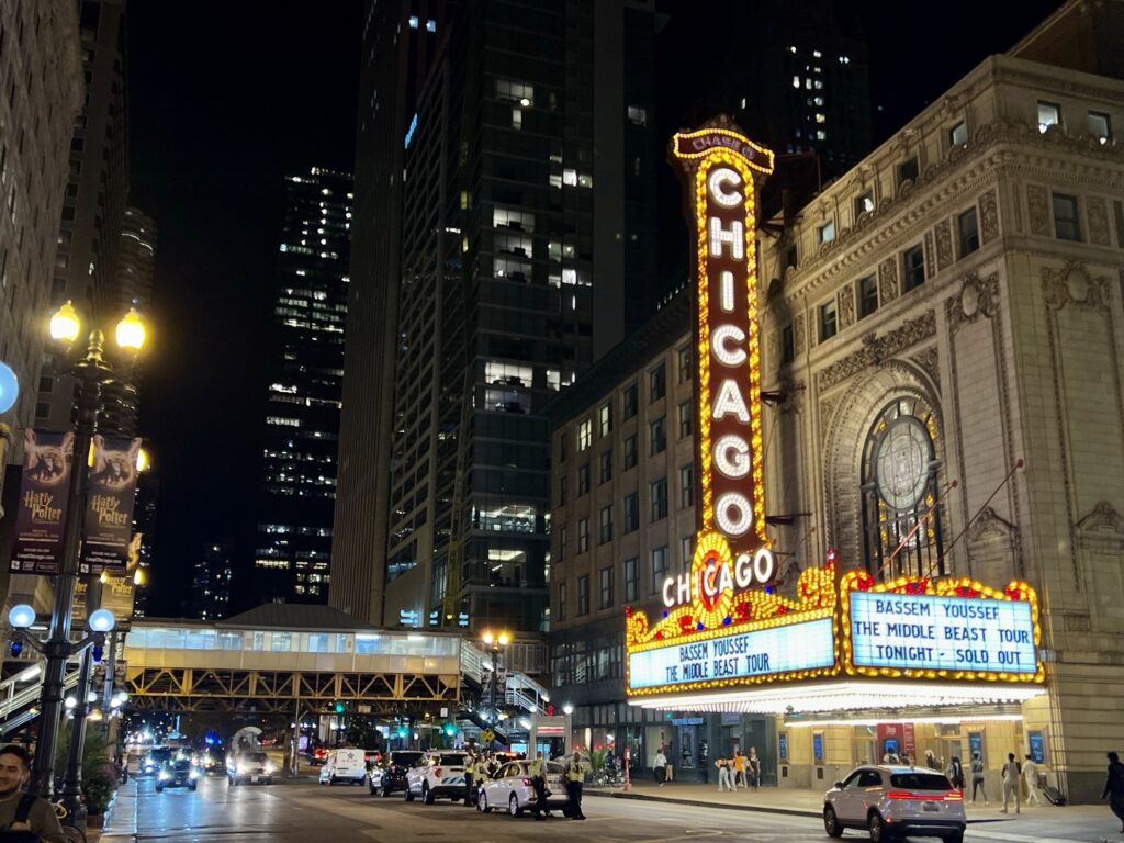 Outside of the Chicago Theatre at night with the skyline view in the background