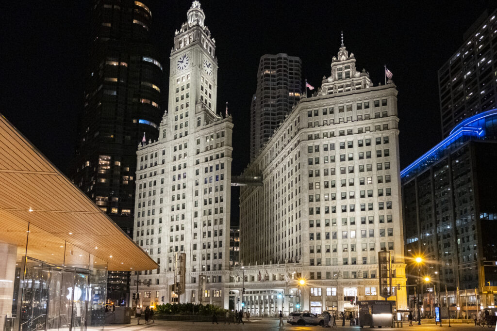 The Wrigley Building in Chicago illuminated at night with the Apple Store on the left side.