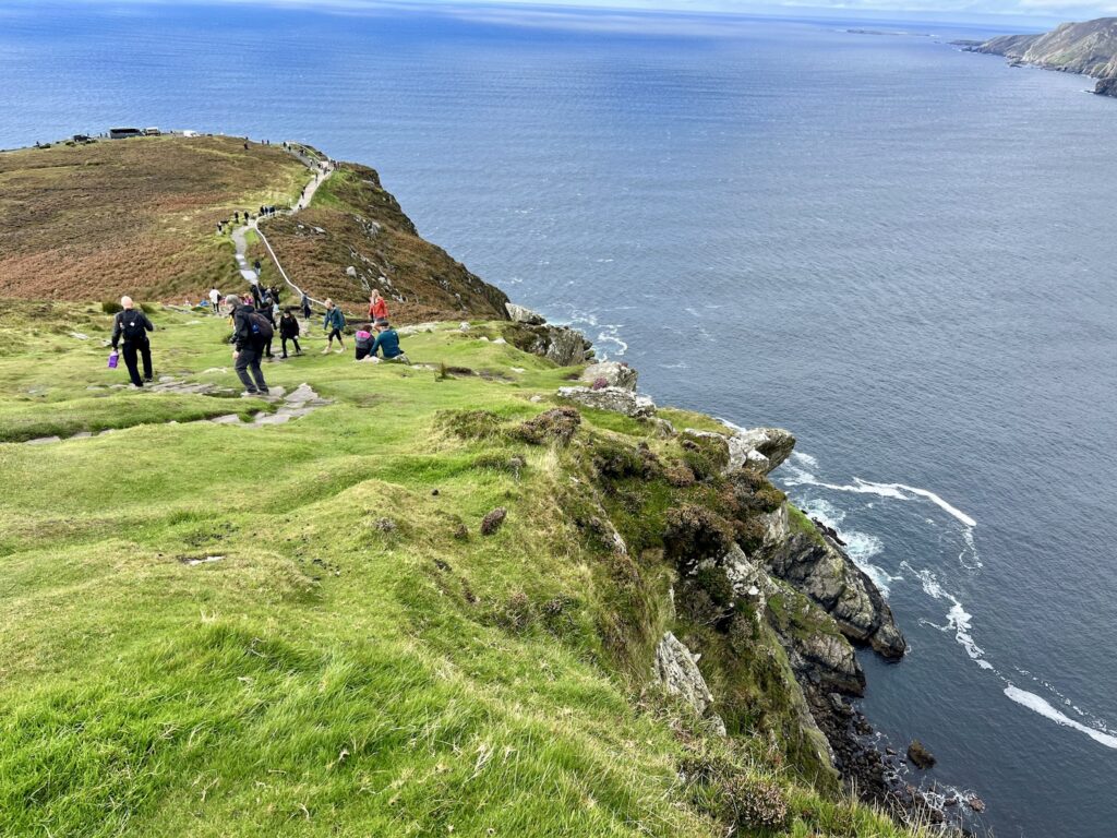 Hikers walking along the edge of Slieve League cliffs in County Donegal, one of the highest sea cliffs in Europe.